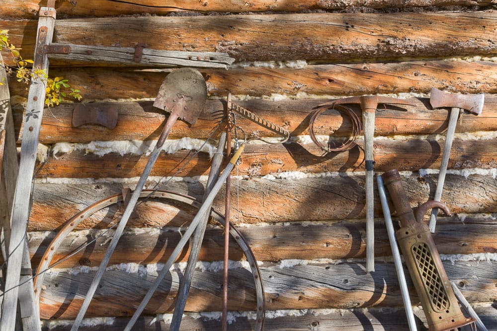 Vintage tools and equipment leaning against a log cabin wall of the Wiseman Trading Post.