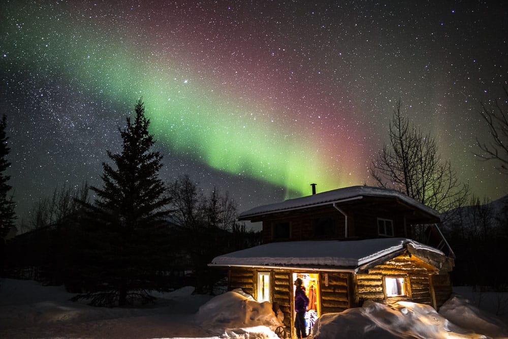 Man views the northern lights from a log cabin